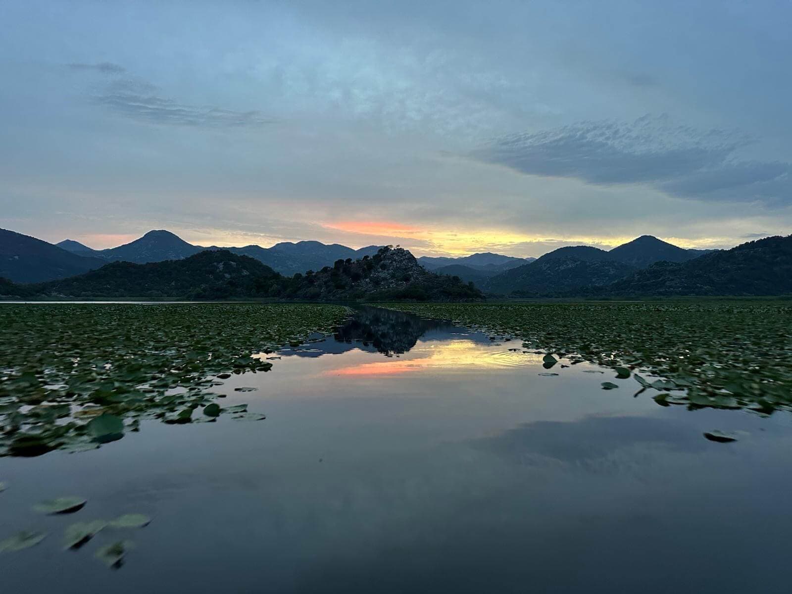 Mountains mirrored in the still water of Lake Skadar at sunset
